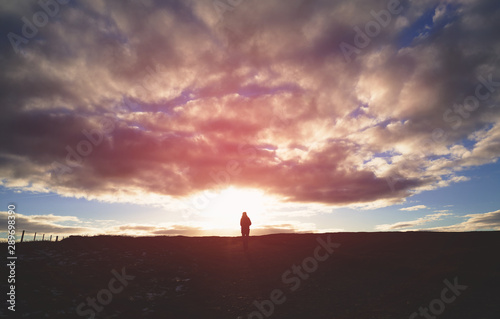 A distant hiker in the centre of the frame walking into a dramatic sunset.