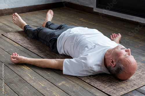 Mature hispanic man in yoga corpse pose in wooden floor. Restorative position after practice.