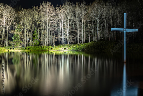 Cross on the water with an inverted reflection in a beautiful nature forest background. light up and illuminated the night photo