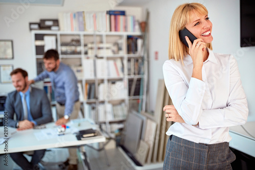 Smiling woman standing in business office and use phone.