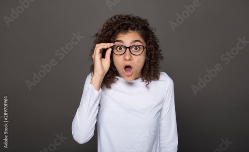 Shock on the girl's face with glasses. Crazy surprise in a young woman on a black background. 