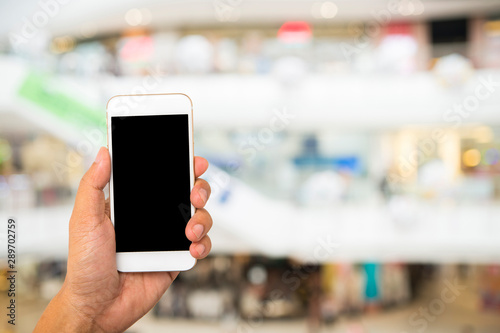 Hand hold black smartphone on blur shopping mall background