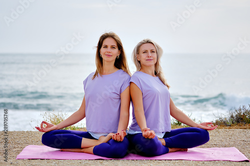 Women sit in lotus pose do yoga exercise meditating on beach near sea