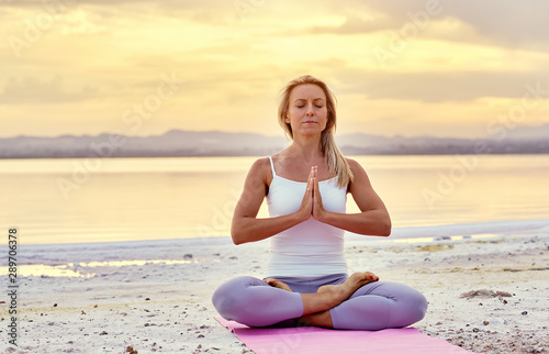Aged woman sitting in lotus position do meditation on nature during sunset