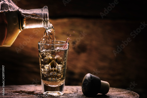 Drink bottle and glass with alcohol content. Image of translucent skull in glass. Alcoholism, addiction or poison concept. photo