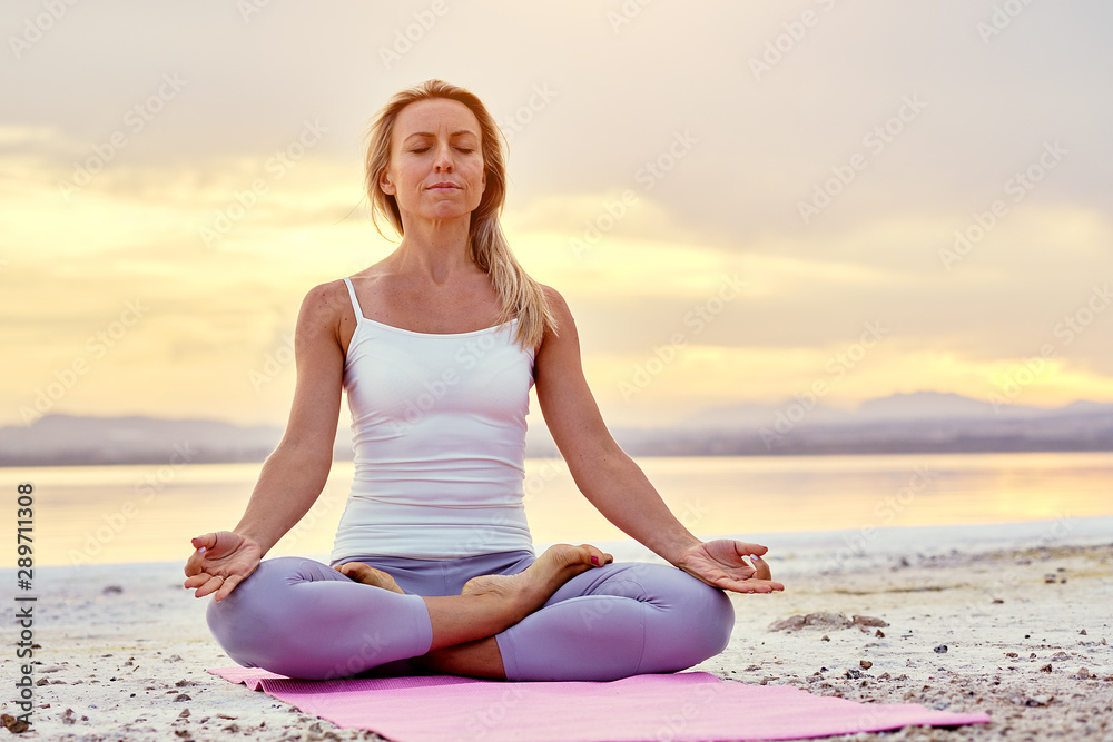 Middle-aged woman seated in lotus pose doing meditation on nature