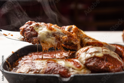 Parmegiana Steak also known as Filet Parmegiana in a black iron pan on a wooden white background, cheese and tomato sauce. Soft light, angle view