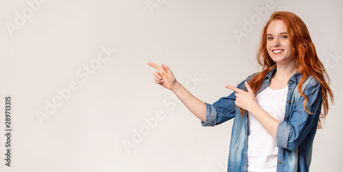 Cheerful teen girl pointing at free space on light background