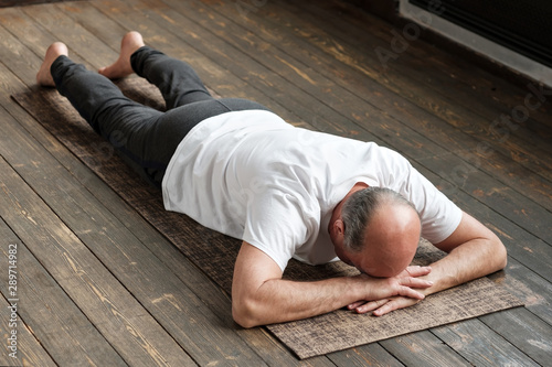 Senior super-ager man resting after yoga exercise on floor. Sports at home for health. Restorative posture.