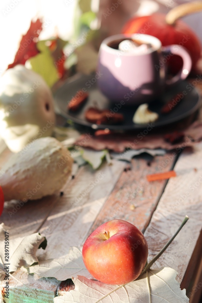 Cup of coffee, rose,  apple, pumpkins, leaves, spices on a wooden surface on a window background, home comfort concept, Thanksgiving, autumn season