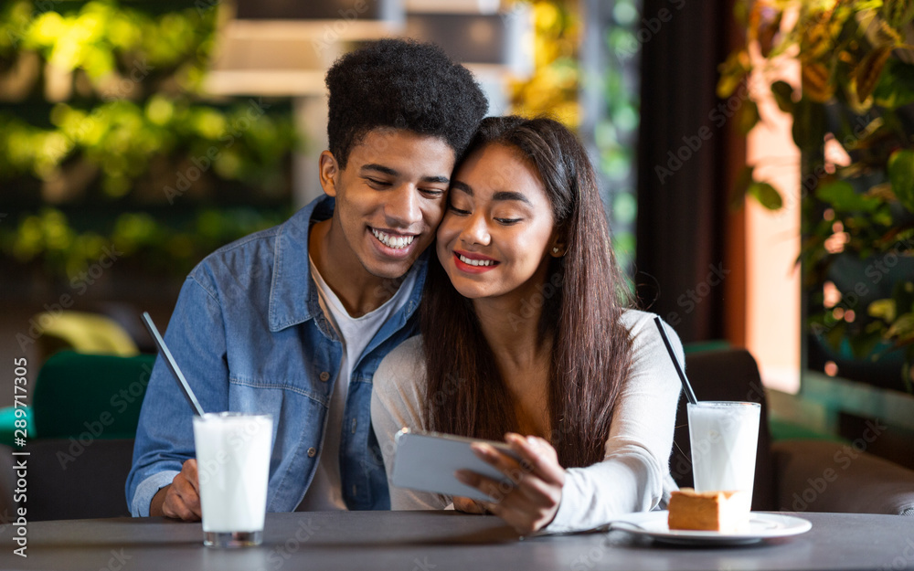 Couple of teenagers watching photos on phone in cafe Couple of teenagers watching photos on phone in cafe