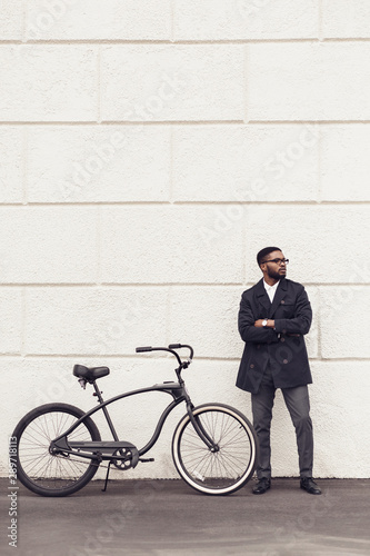 Young african man with bicycle standing over white wall
