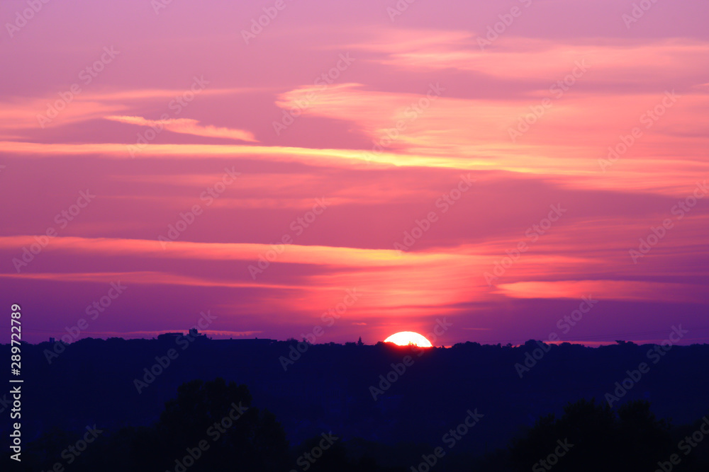 Close up on the sun rising in a sky with pink and purple gradient colors. Silhouette of the horizon with isolated trees. Flaming sky at sunrise. Close up on the sun rising in a sky with pink and purple gradient colors. Silhouette of the horizon with isolated trees. Flaming sky at sunrise.