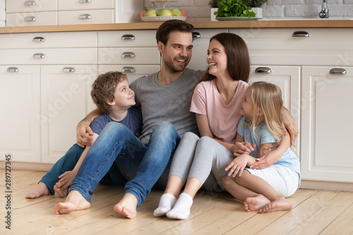 Happy family of four sitting on wooden floor at kitchen.