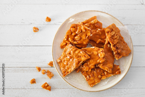 Plate of traditional peanut brittle candy pieces. Top view on a white wood background. photo
