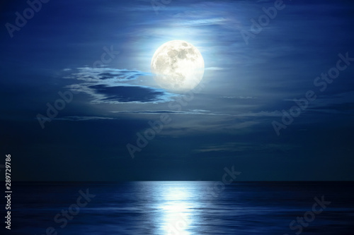 Super full moon and cloud in the blue sky above the ocean horizon at midnight, moonlight reflect the water surface and wave, Beautiful nature landscape view at night scene of the sea for background