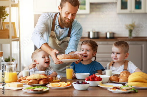 happy family father with children feeds his sons and daughter in kitchen with Breakfast