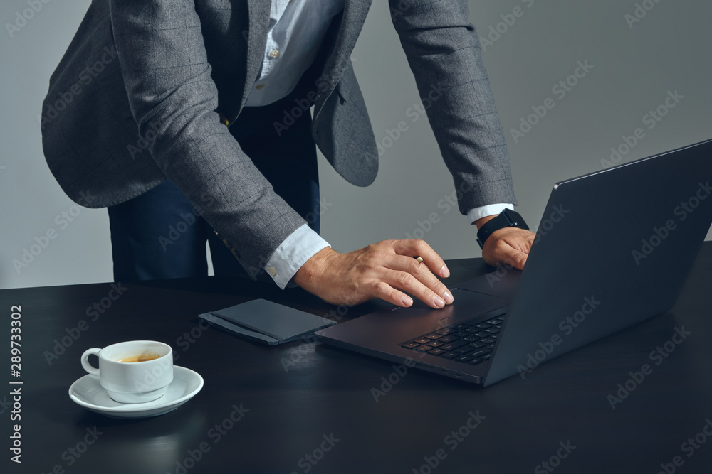 Close-up shot of businessman hands, he is working at a laptop in office, gray background. Dressed in a classic suit and white shirt. Close-up shot of businessman hands, he is working at a laptop in office, gray background. Dressed in a classic suit and white shirt.