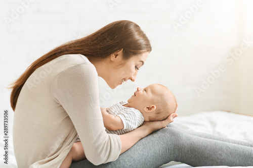 Young mother playing with adorable baby in bed
