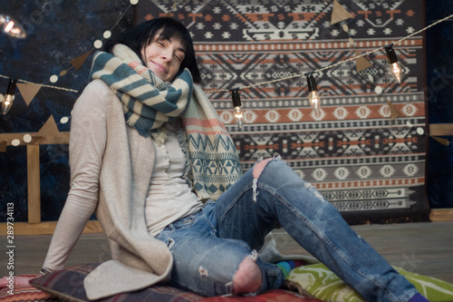 Beautiful girl in a warm scarf against the background of a minimalist Scandinavian interior and garlands, Christmas and New Year concept, selective focus