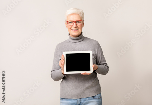 Friendly senior woman demonstrating blank screen on digital tablet