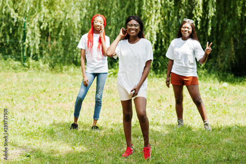 Three african american womans in park at white t-shirts.