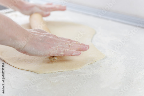 Сook rolls out the dough with rolling pin on white background. Cooking in the kitchen baking. Female hands are holding rolling pin sprinkled with flour. Chef at work on pizza.