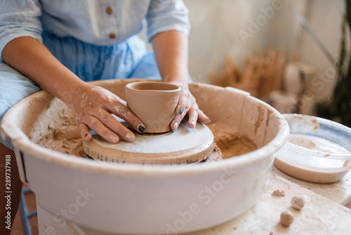 Female master holds wet pot over the pottery wheel