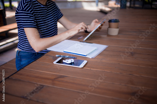 Feemale reelancer, with large wrist watch, works at a wooden table on tablet, with gadgets and papers. photo