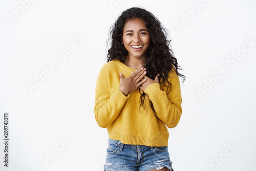 Pleased and flattered cute smiling african american curly-haired girl, wear yellow cozy sweater, press hands to chest, feeling grateful thanking for help, grinning appreciate lovely gift photo