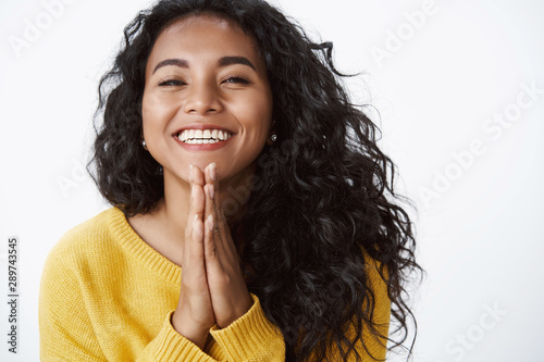 Happy grateful young cute african american girl thanking for help, very glad receive lovely gift, smiling joyfully, press palms together in pray, standing white background in yellow sweater