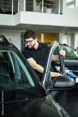 Visiting car dealership. Handsome bearded man is stroking his new car and smiling © F8  \ Suport Ukraine
