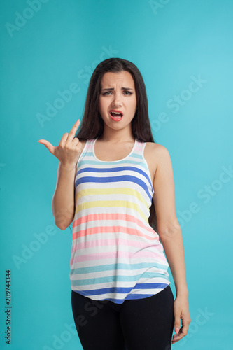 Brunette woman with long hair  dressed in striped shirt and black leggings  posing against blue studio background. Sincere emotions. Close-up.