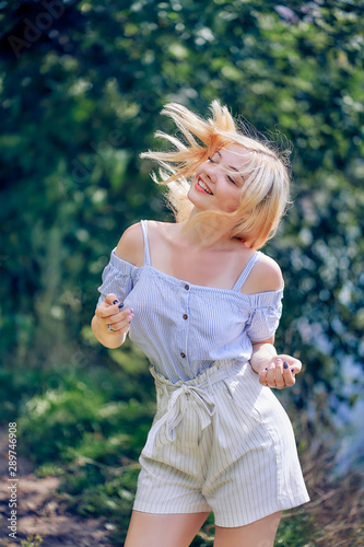 portrait of a beautiful blonde girl on a background of foliage in a blue dress