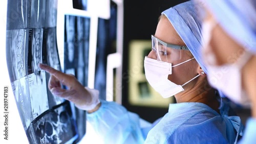 Doctor examines x-ray , holding it in hands indoors. Doctors working together in the office, they are examining a patient's x-ray and discussing diagnosis and treatment
