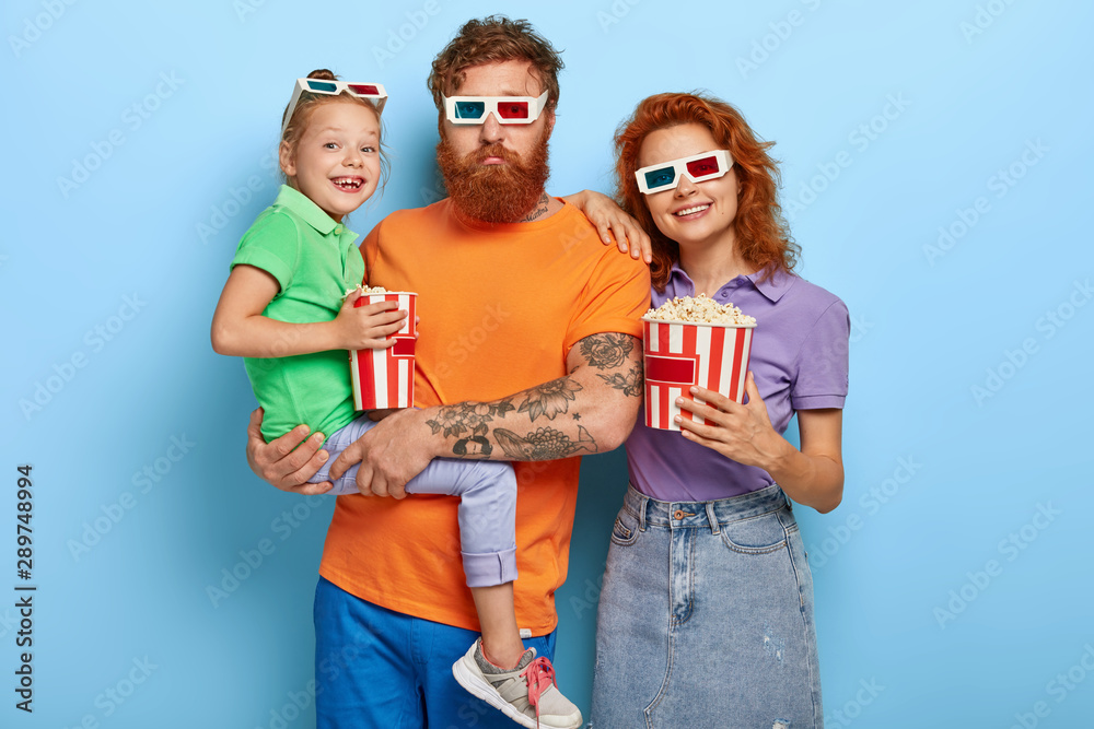 Φωτογραφία Horizontal shot of happy ginger family spend free time in cinema, come on premier of film, eat salty popcorn
