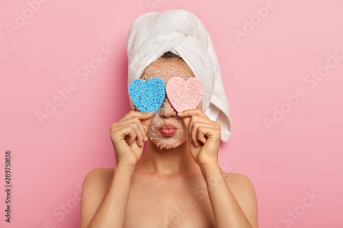 Fotografie, Obraz Close up portrait of lovely woman hides face with two cosmetic sponges, has lips