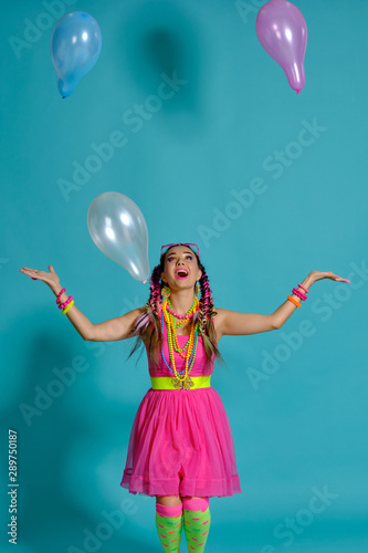 Lovely girl with a multi-colored braids hairstyle and bright make-up, posing in studio with air balloons against a blue background. © nazarovsergey