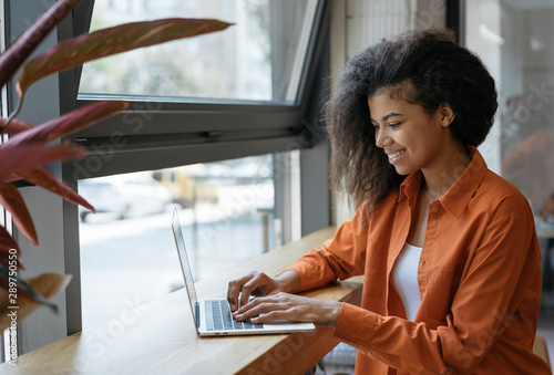 Happy African American woman copywriter working freelance project in modern cafe. Businesswoman using laptop, searching information on website. Successful business. Online training courses concept photo