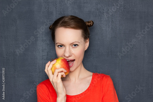 Portrait of cute girl biting ripe red apple with appetite