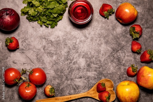 Fresh organic red themed fruit  vegetables  wine  and wooden heart shaped spoon  laying on concrete background countertop. Captured from above. 