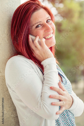 Cute smiling redheaded woman making a call with her cell phone