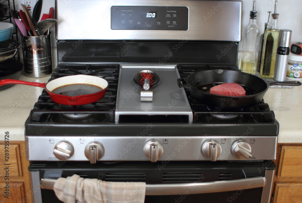 Ahi tuna steak searing in a cast iron skillet next to an enameled skillet with demiglace, on a