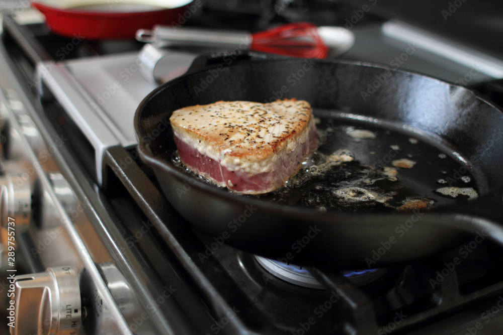 Ahi tuna steak searing in a cast iron skillet on a gas stove. Ahi tuna steak searing in a cast iron skillet on a gas stove.