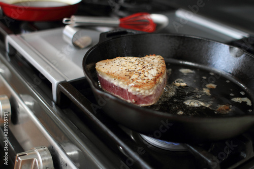  Ahi tuna steak searing in a cast iron skillet on a gas stove.