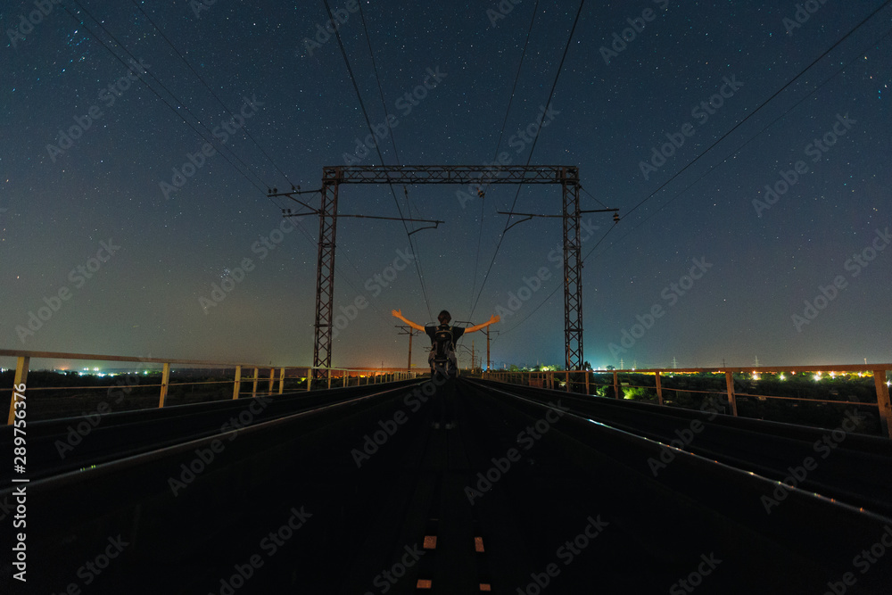 Traveler staying in pose of faith between railways and watching starry sky