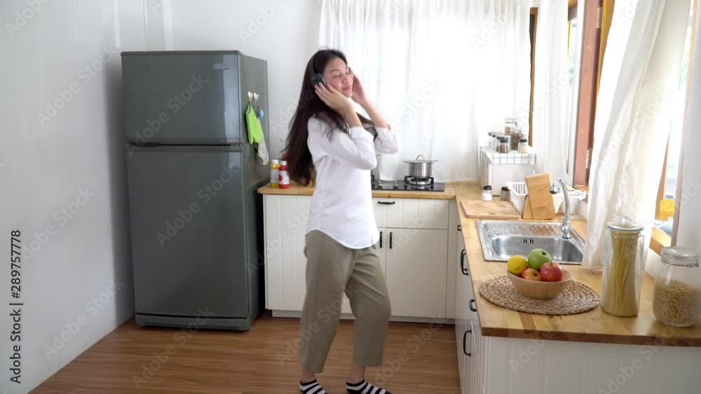 4K Wide shot of happy beautiful young asian woman listening music from headphone and dancing at home kitchen in the morning. Pretty teenage girl start fresh day by dancing and listening the music. 4K Wide shot of happy beautiful young asian woman listening music from headphone and dancing at home kitchen in the morning. Pretty teenage girl start fresh day by dancing and listening the music.