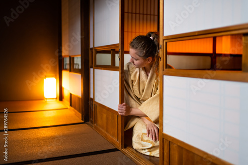 Traditional Japanese home ryokan room with gaijin caucasian woman in kimono, tabi socks opening shoji sliding paper doors sitting on tatami mat floor photo