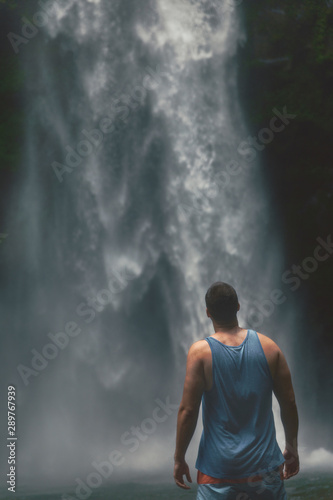 Back view of young man standing in front of powerful Nungnung waterfall on Bali