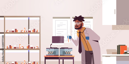 scientist holding test tubes with blood samples african american man in uniform using analyzer medical machine research science medicine concept modern laboratory interior portrait horizontal